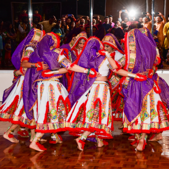 Dancers in purple and red traditional Indian dress performing together at an evening event.